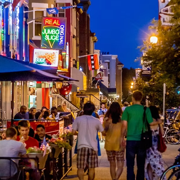 People dining at outdoor restaurant tables on a lively city street at night